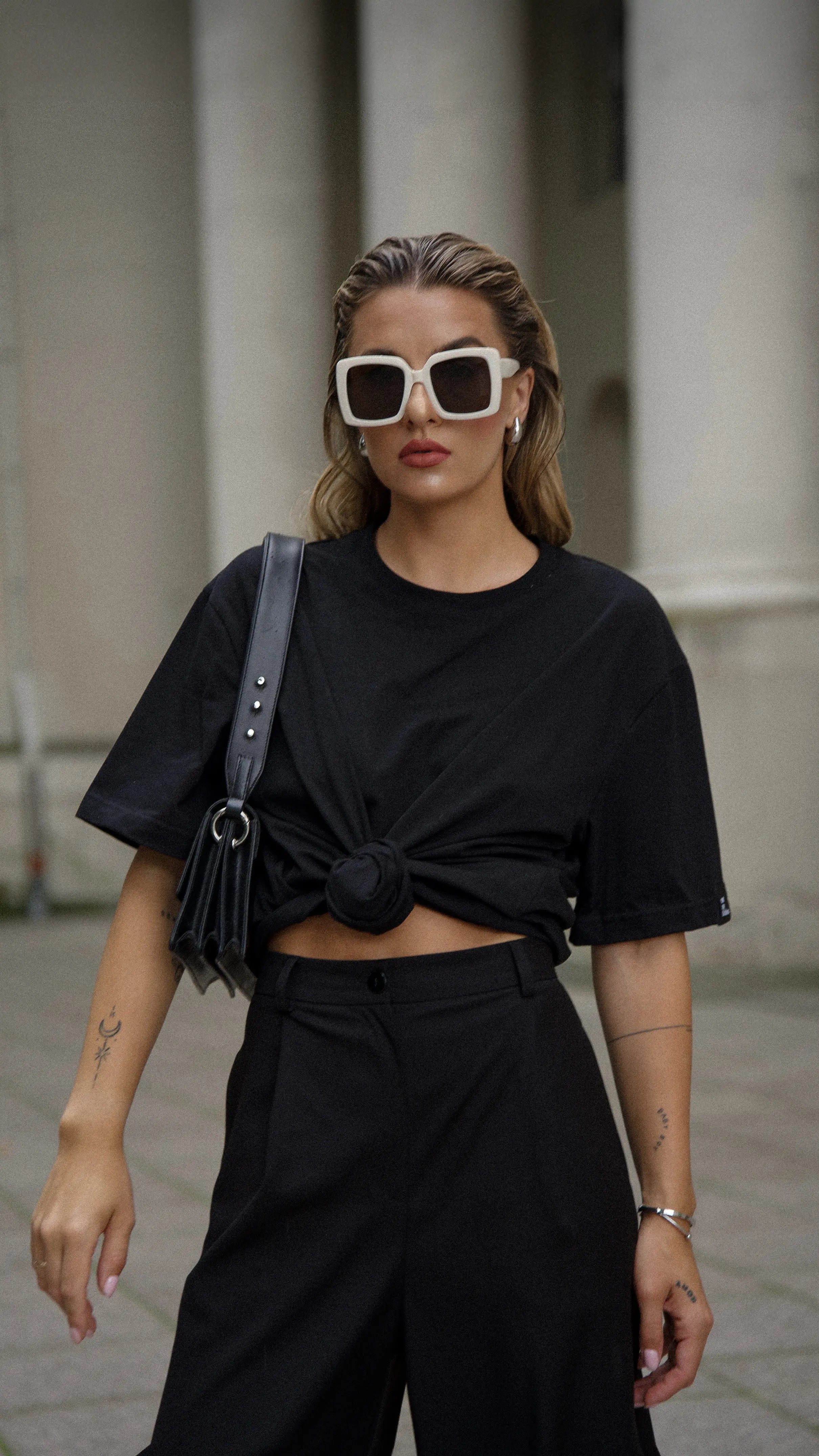 Mergina dėvi juodus cutmyfashion oversized stiliaus laisvalaikio marškinėlius ir juodas platėjančias klasikines kelnes