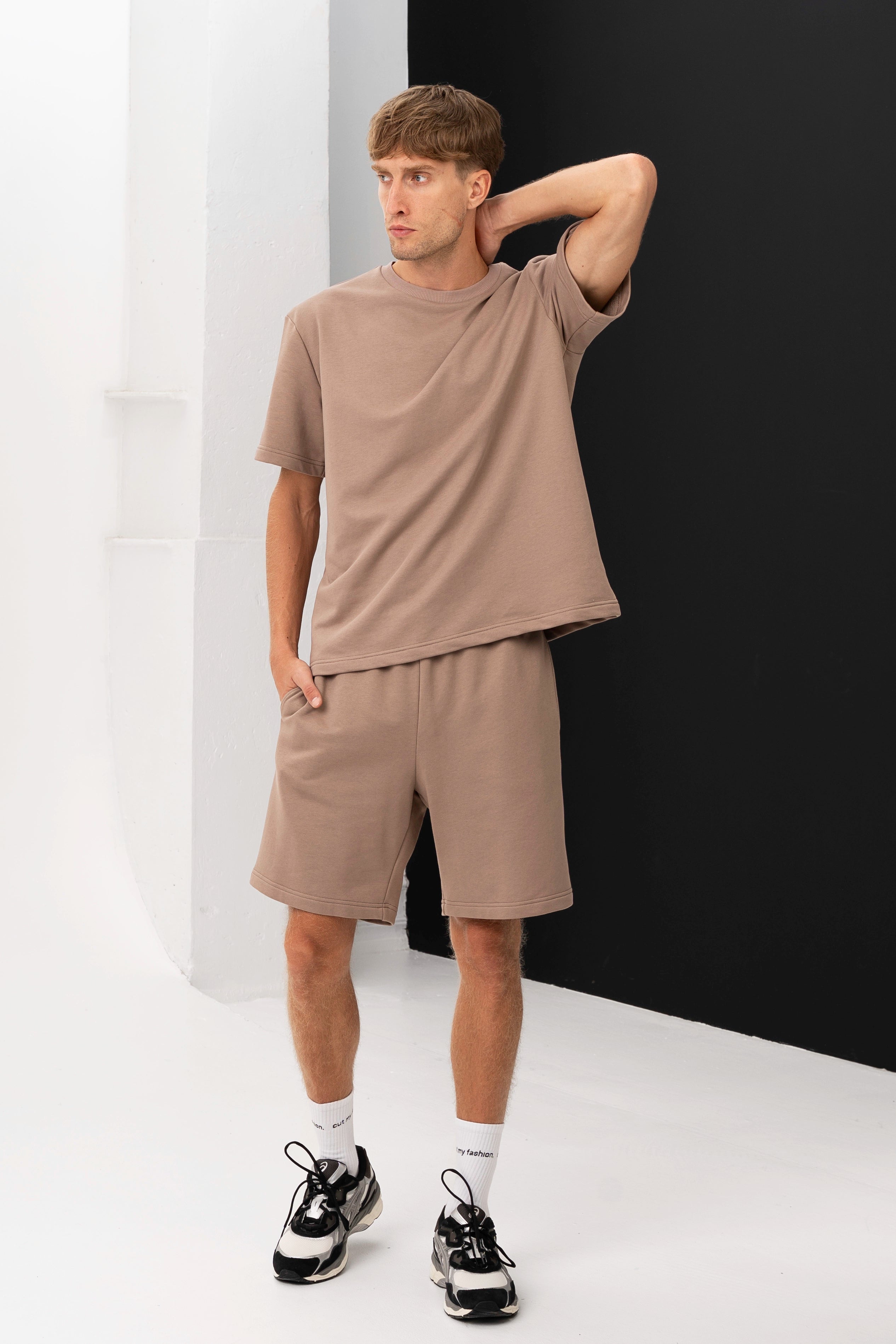 Šoninis vaizdas į vyrą, vilkintį laisvalaikio komplektą su marškinėliais ir šortais, žiūrintį į tolį