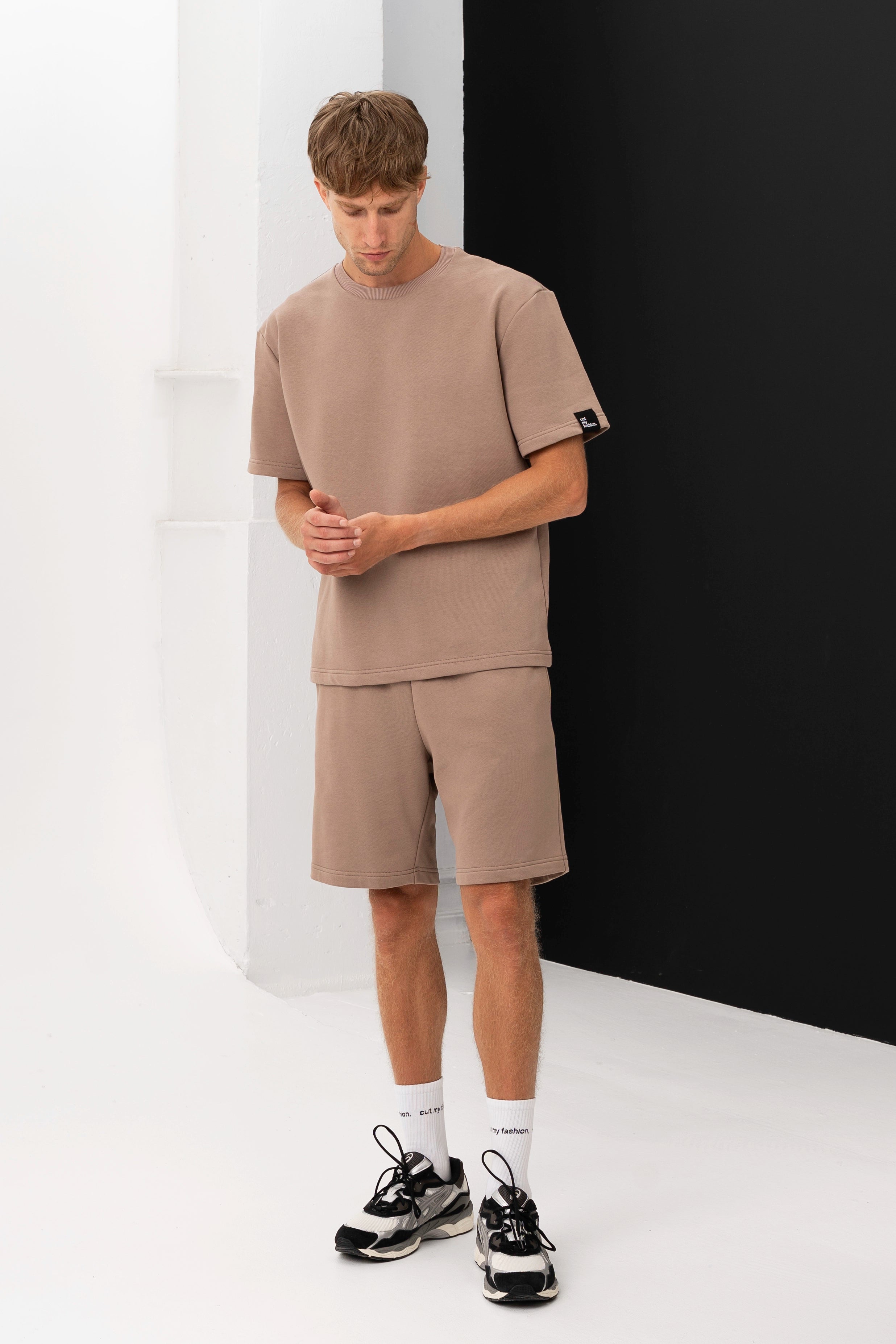 Vyriškas laisvalaikio drabužių derinys – marškinėliai ir šortai iš minkšto audinio, pozuojama juodame ir baltame fone