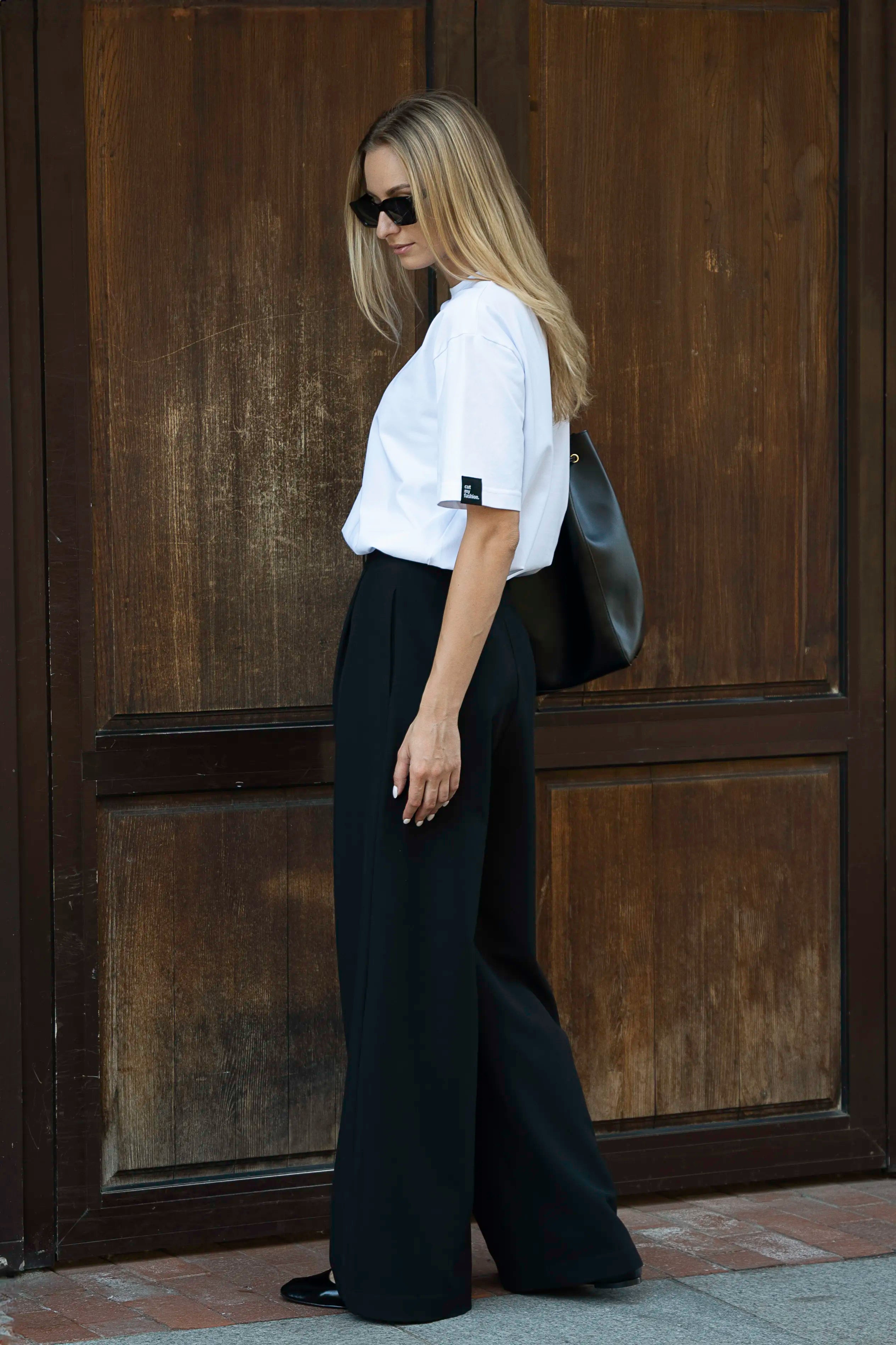 Ein weißes Damen-T-Shirt im Oversize-Stil und eine schwarze klassische Hose von der Seite