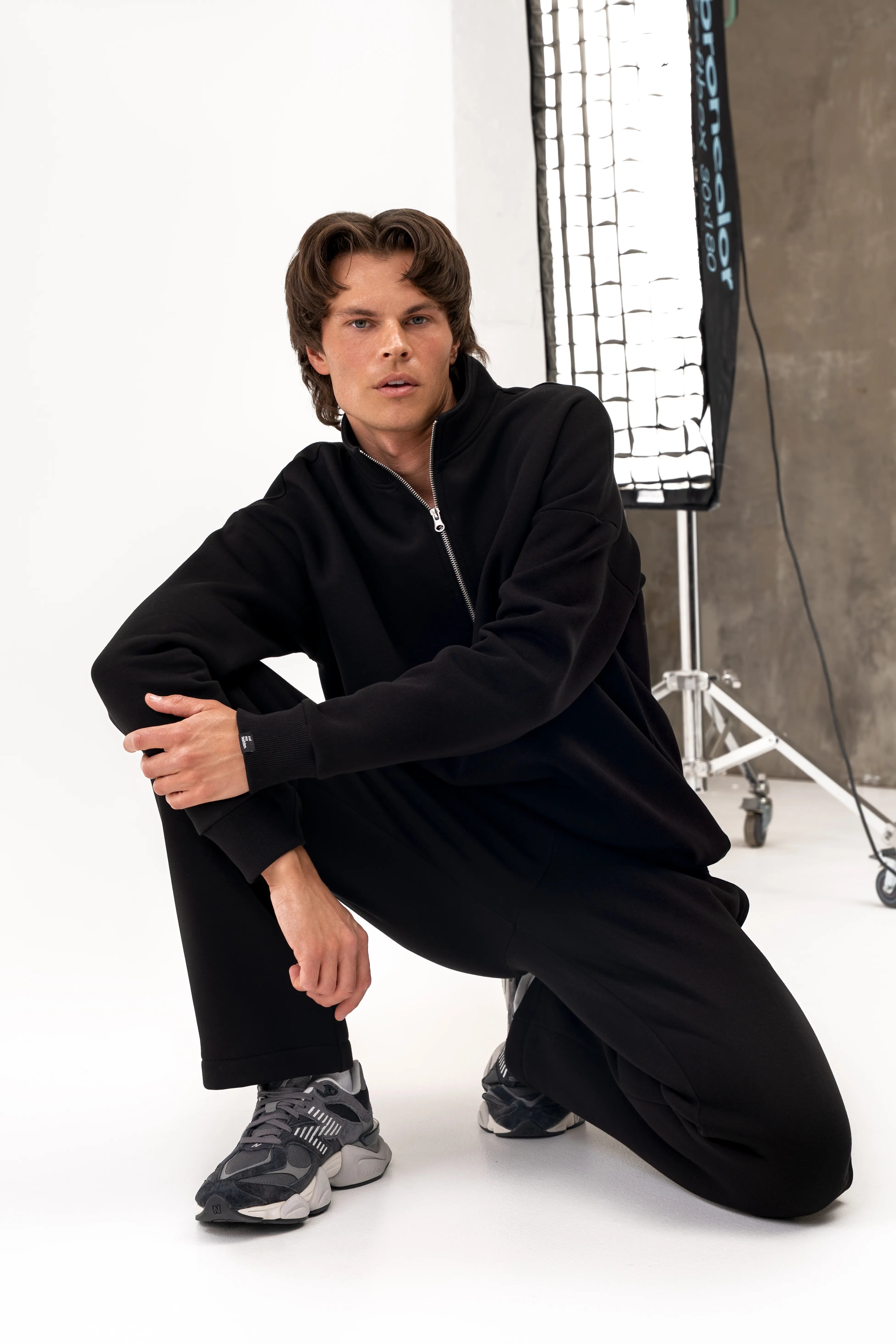 Vyras pritūpęs vilki juodus laisvalaikio treningus „Vilius“ su aukšta apykakle ir tiesiomis kelnėmis su kišenėmis