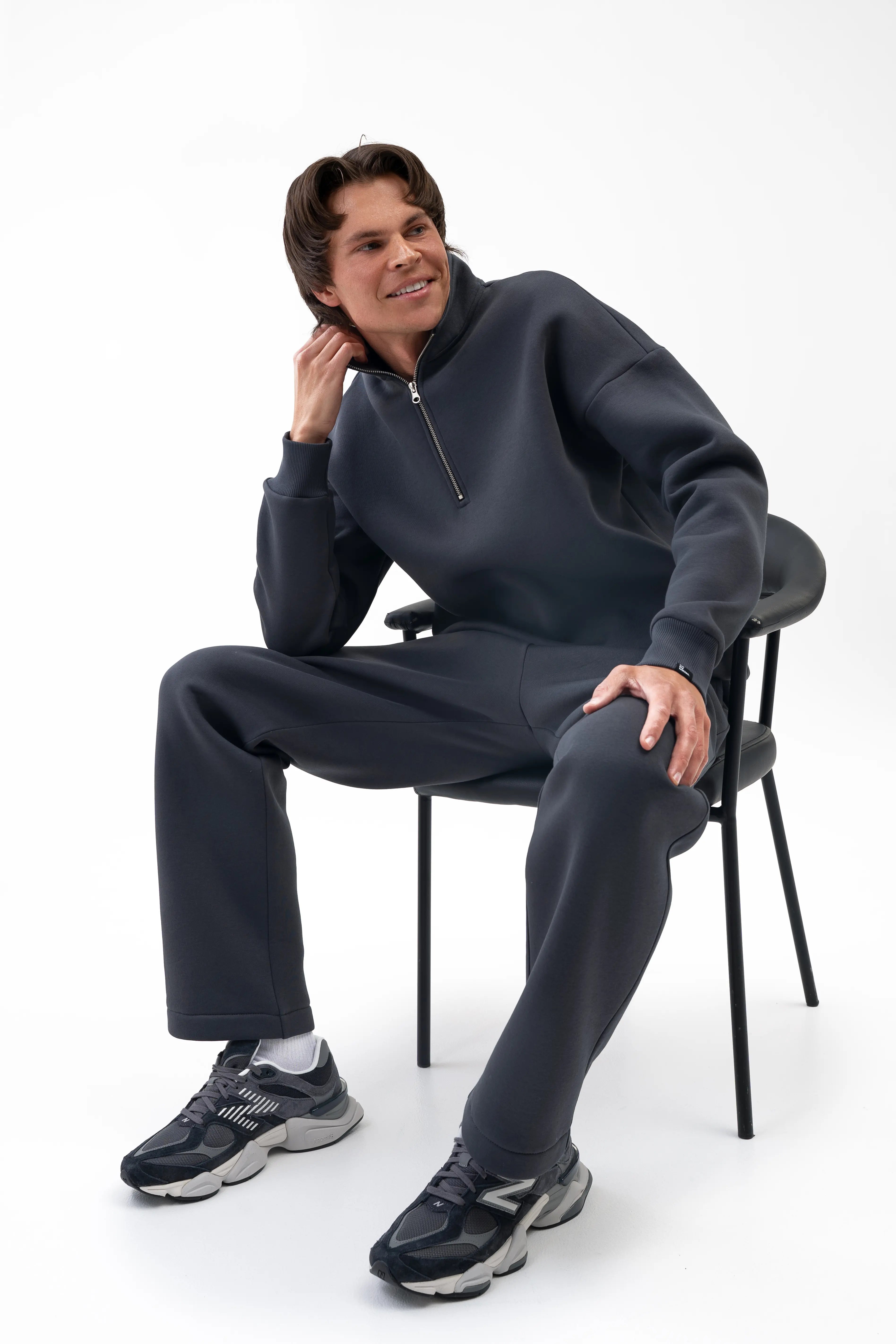 Vyriškas iron spalvos kostiumėlis su aukšta apykakle ir tiesiomis kelnėmis, modelis sėdi ant kėdės