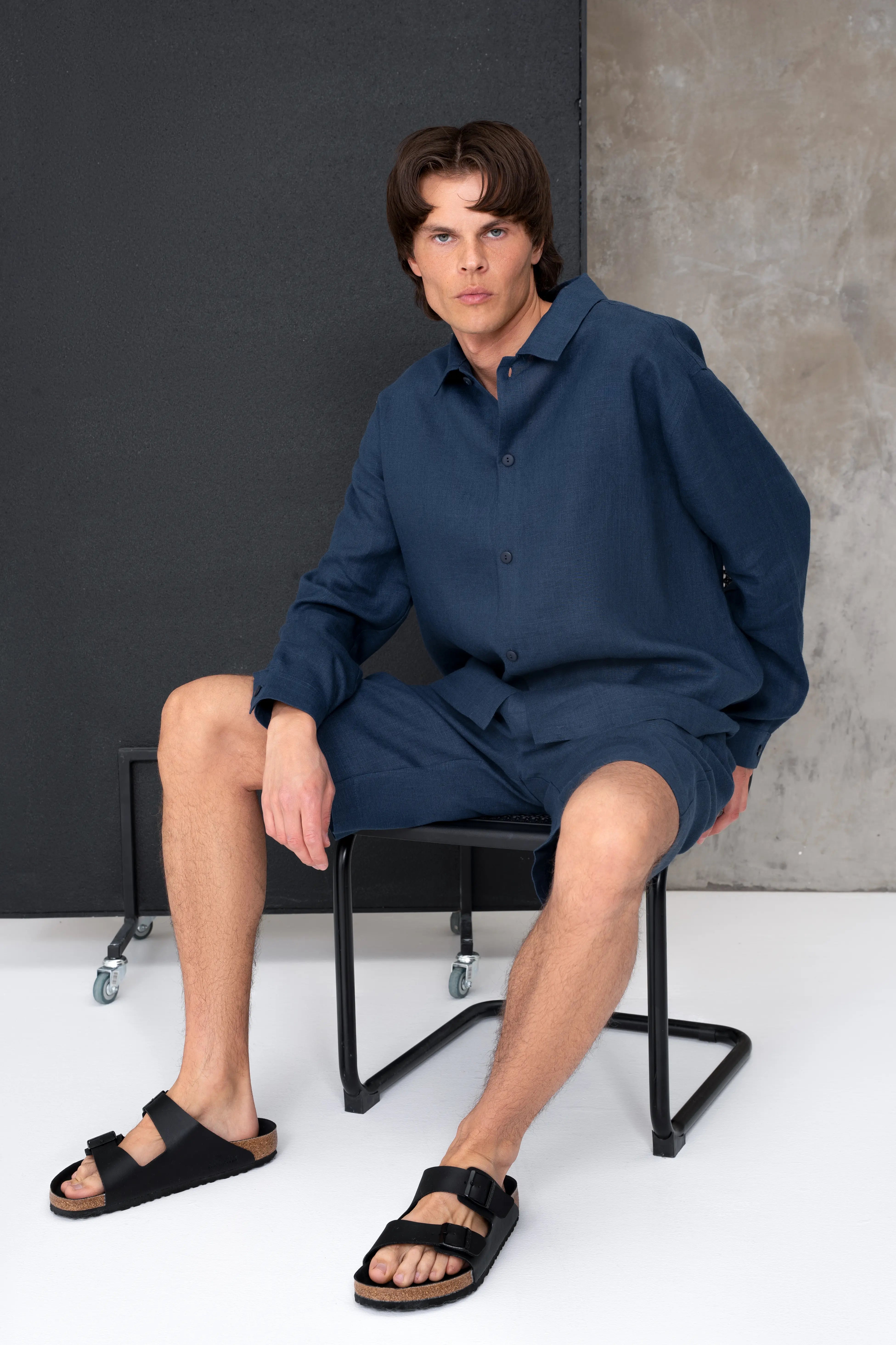 Ein blauer Herrenanzug aus Leinen mit Hemd und Shorts; das Model sitzt auf einem Stuhl