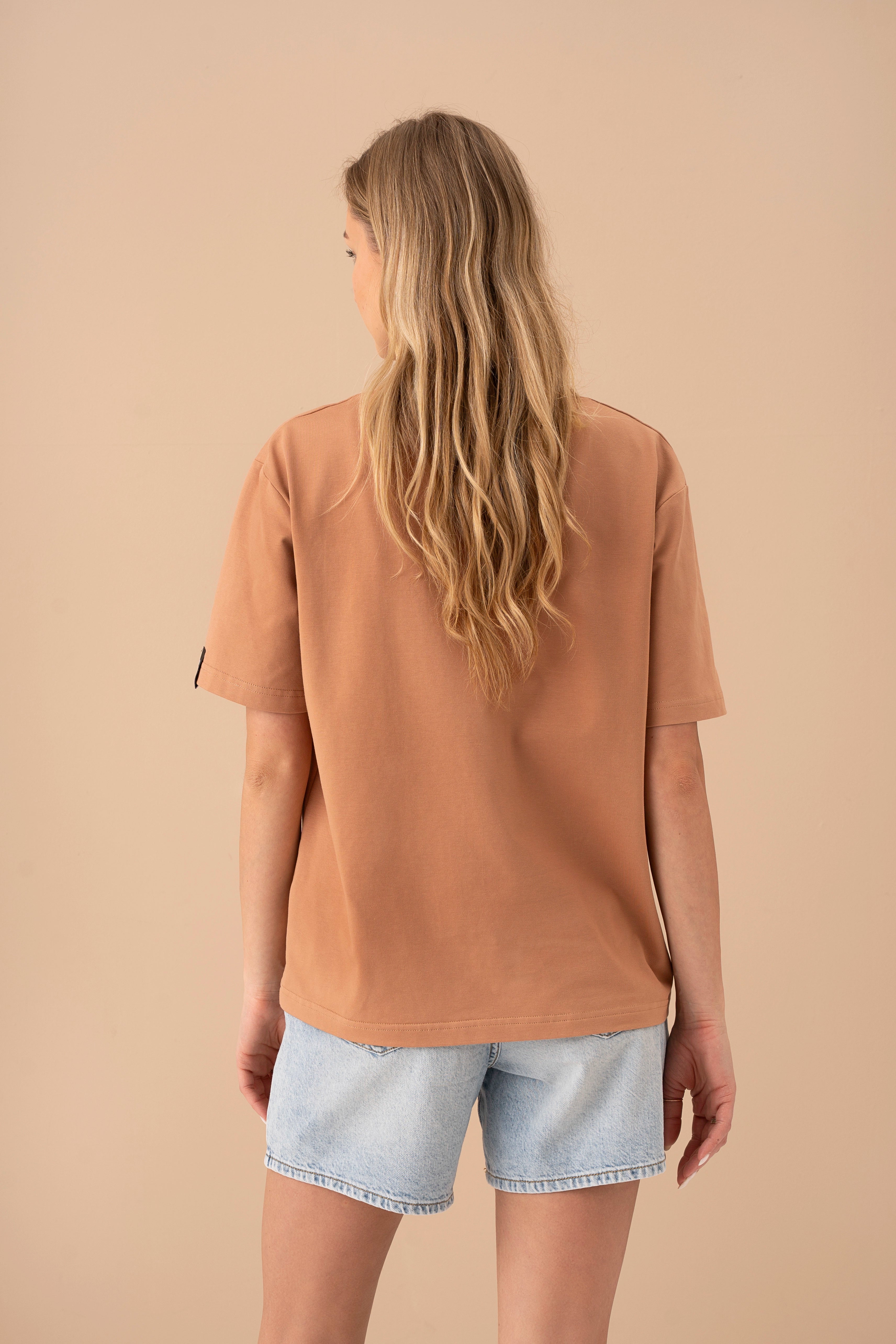 modelis su šviesiais džinsiniais šortais ir mocha spalvos oversized marškinėliais atsisukusi nugara, studijos fonas