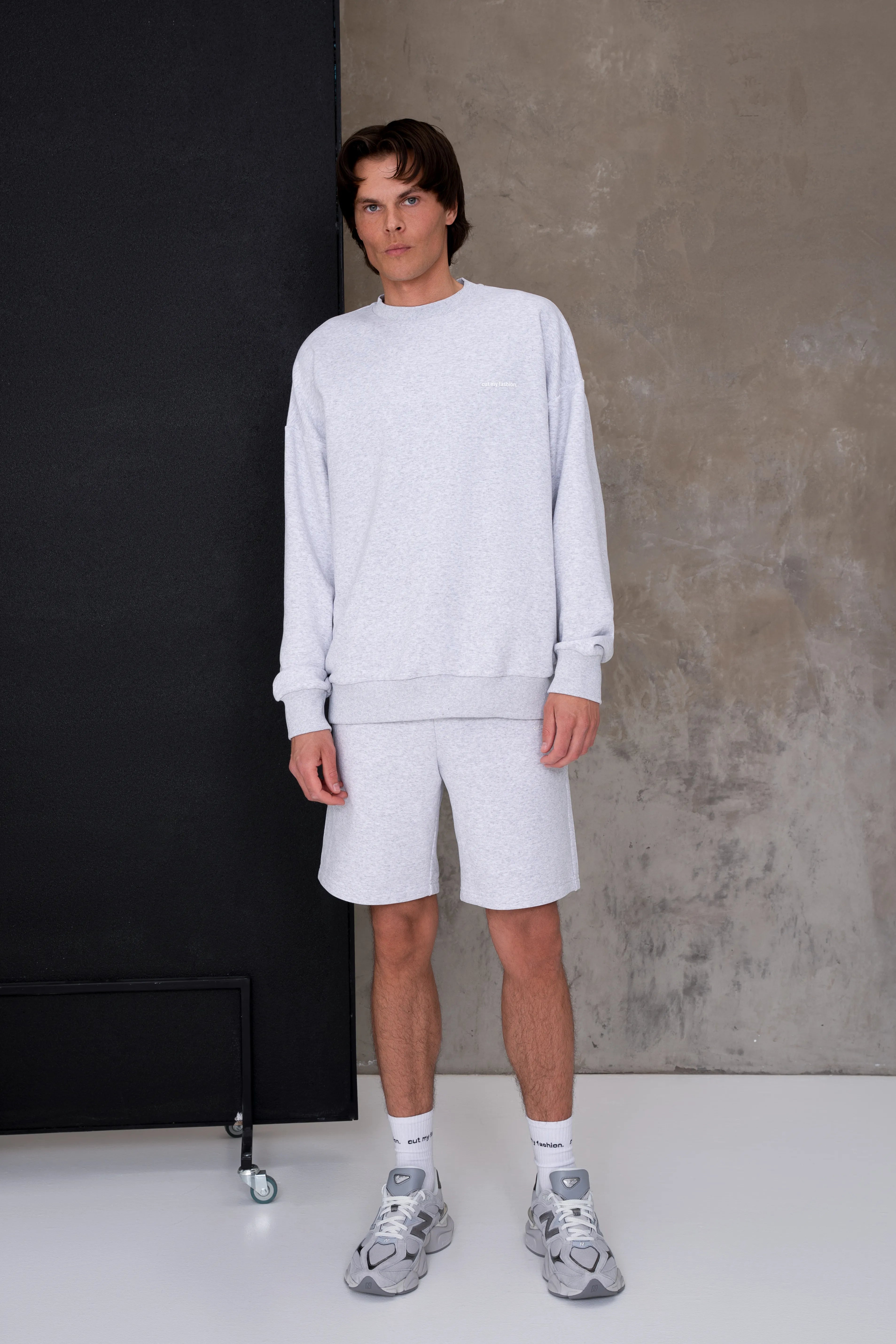 Šviesiai pilkas vyriškas laisvalaikio treningas su šortais, laisvesnio kirpimo džemperis su apvalia apykakle ir ribo apačia, tiesaus silueto šortai su elastingu liemeniu
