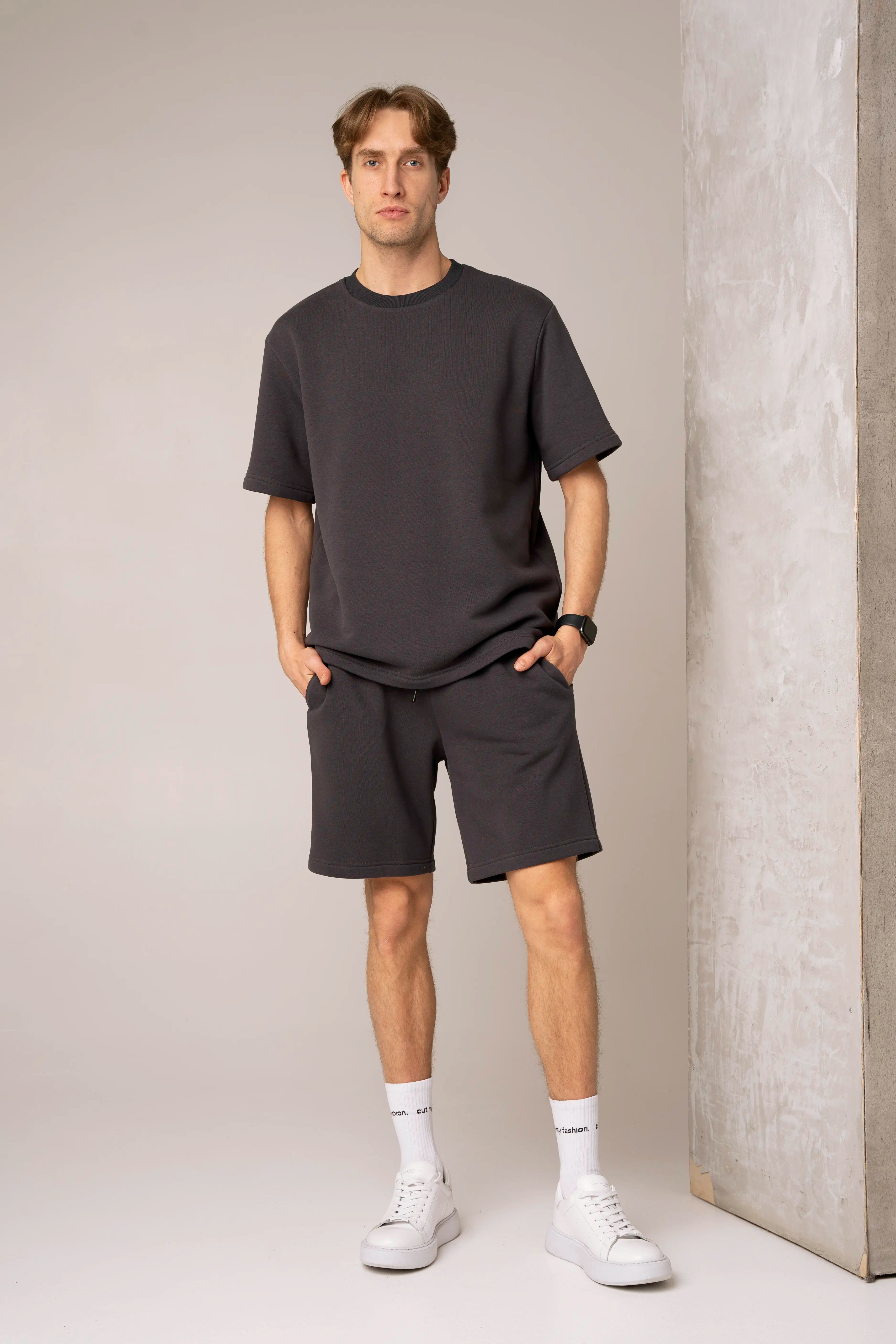 Tamsiai pilkos spalvos vyriškas laisvalaikio treningas su trumpomis rankovėmis, apvalia apykakle, laisvais šortais su kišenėmis ir elastingu juosmeniu.