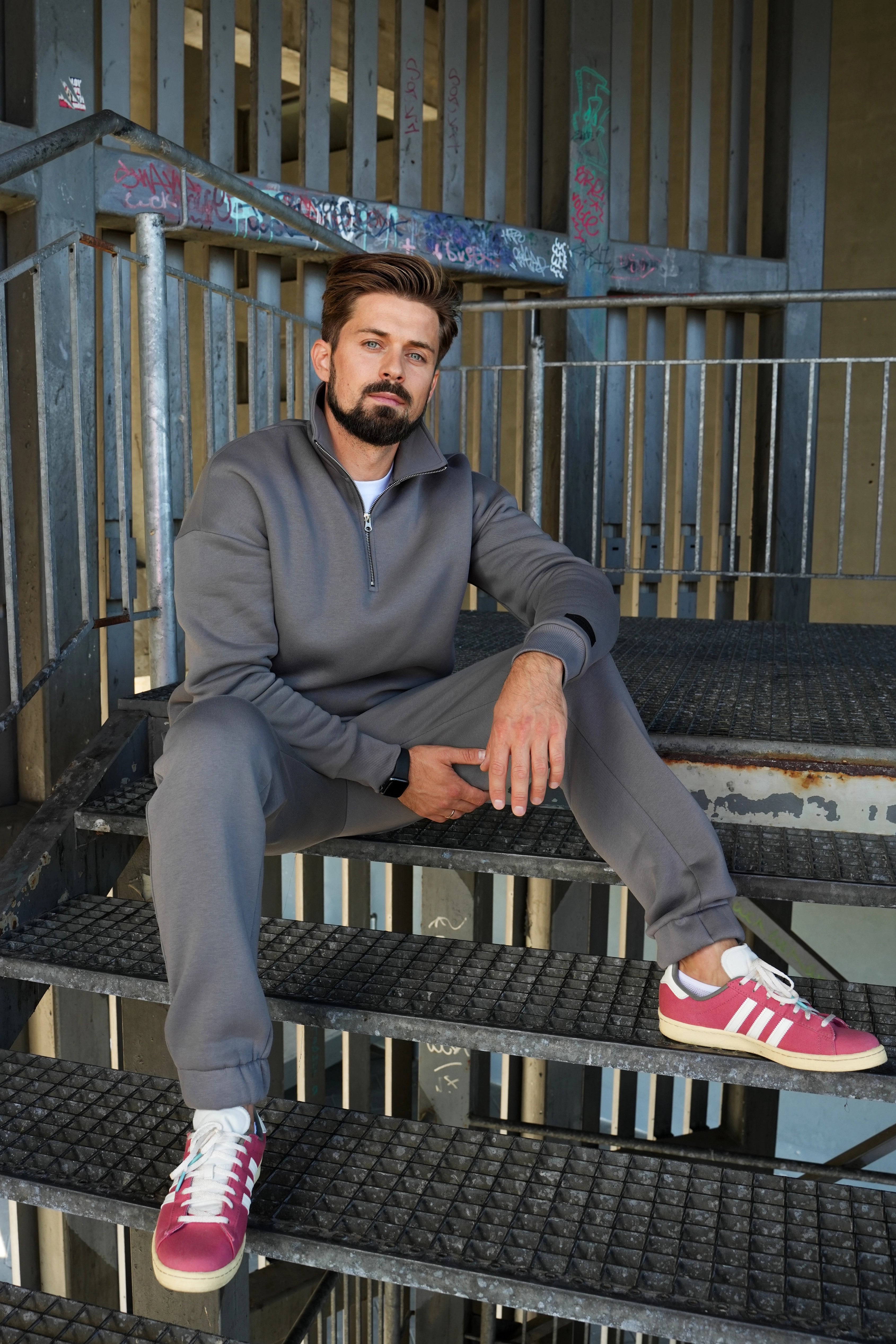 modelis vilki pilkus treningus, sėdi ant metalinių turėklų urbanistinėje aplinkoje, dėvi bordo sportbačius