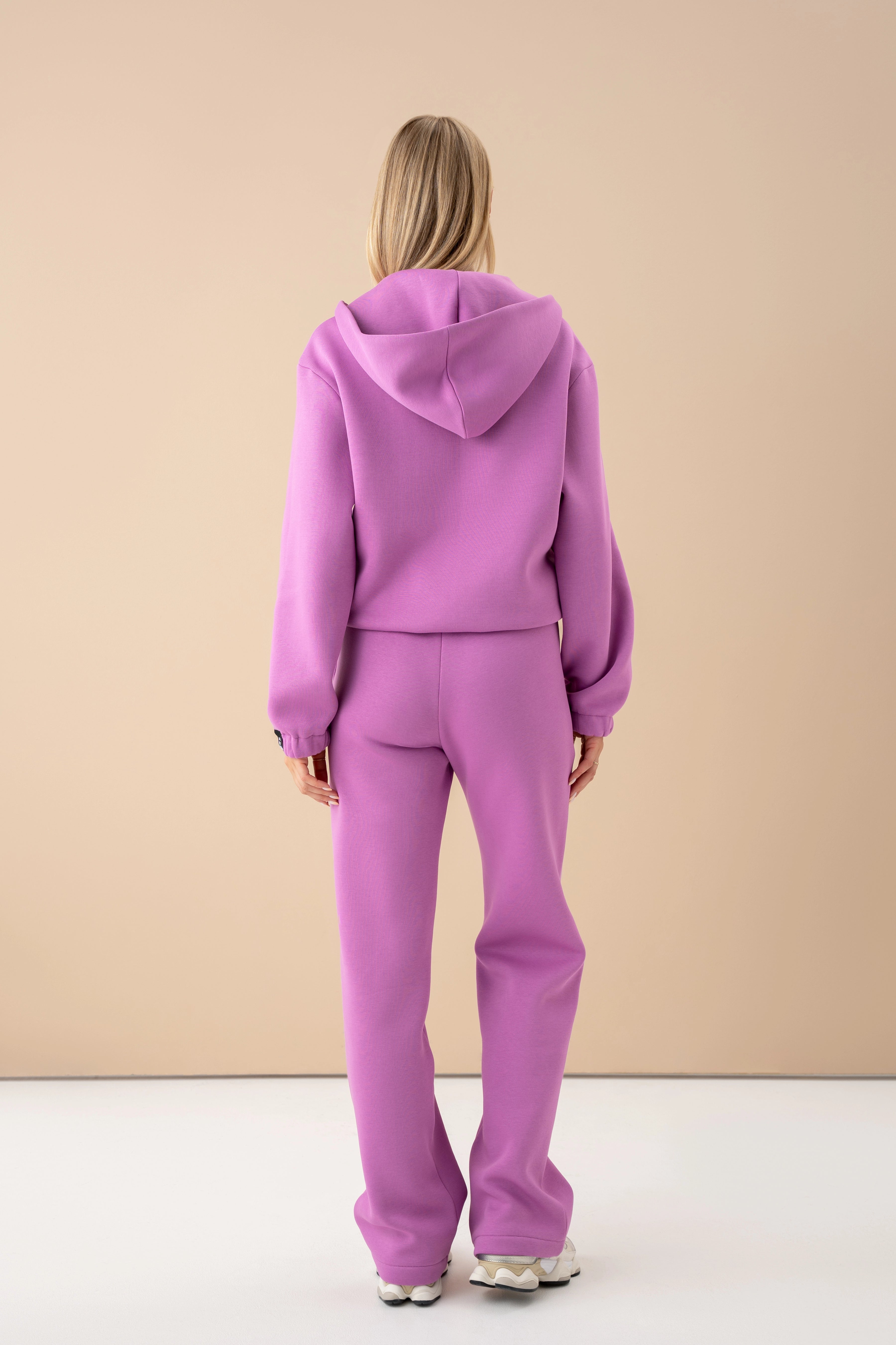 modelis su pastelinės rožinės spalvos džemperiu ir kelnėmis atsisukusi nugara į kamerą, cutmyfashion apranga studijoje