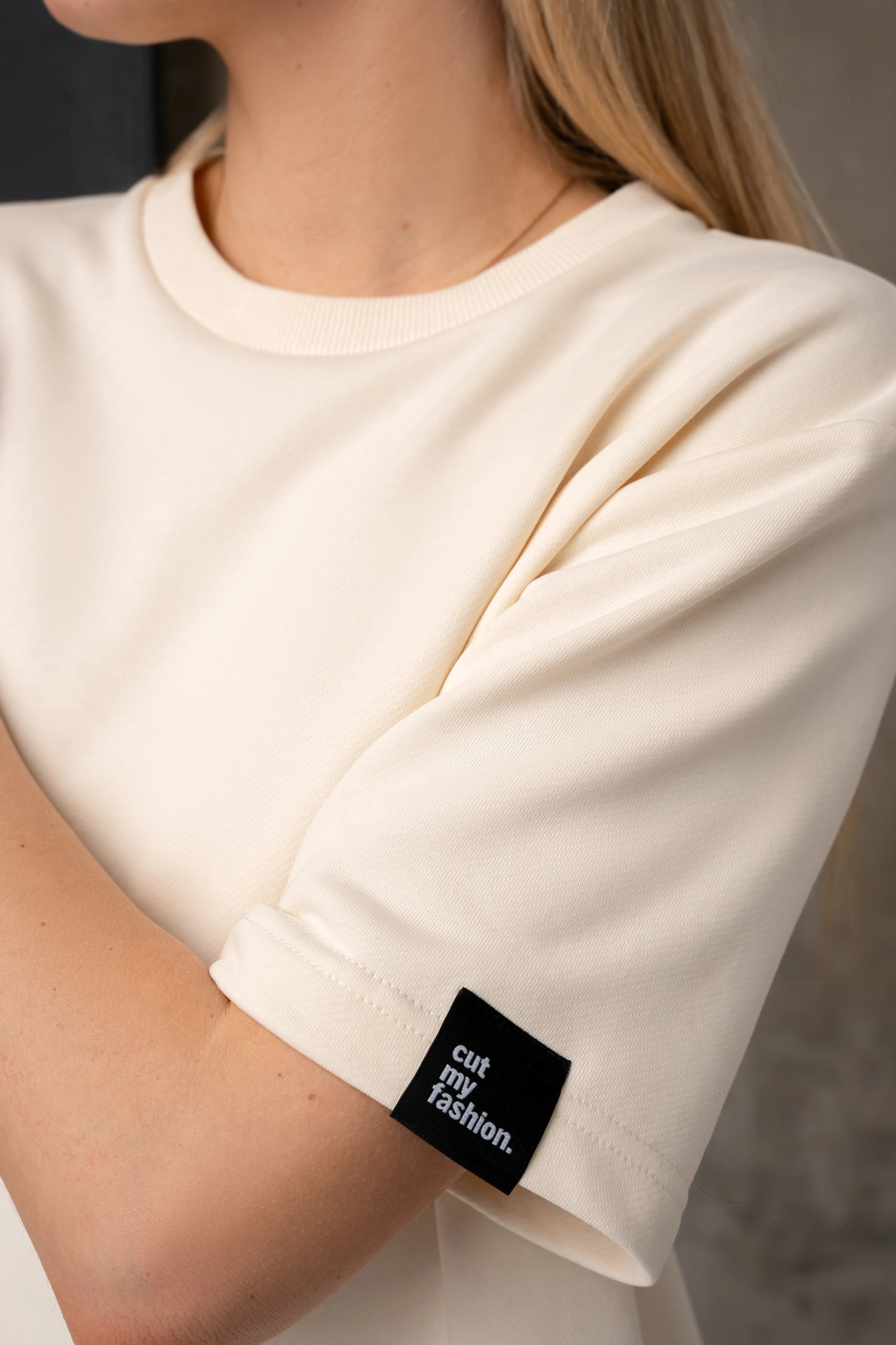 Detail an den Ärmeln einer milchweißen Bluse mit schwarzem „cutmyfashion“-Logo