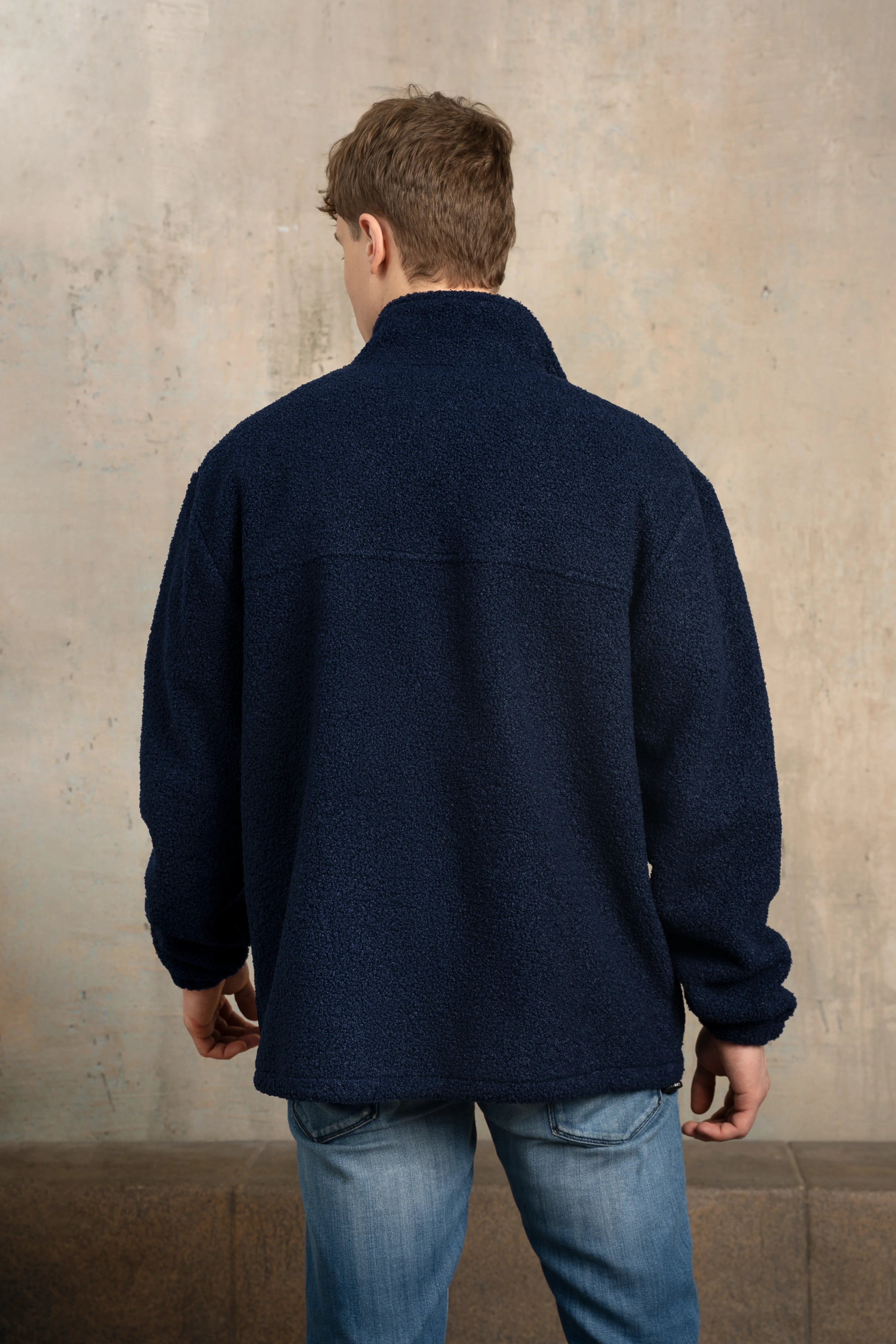 Tamsiai mėlynos spalvos vyriškas džemperis iš nugaros su stačia apykakle, ilgomis rankovėmis ir tiesia nugaros linija