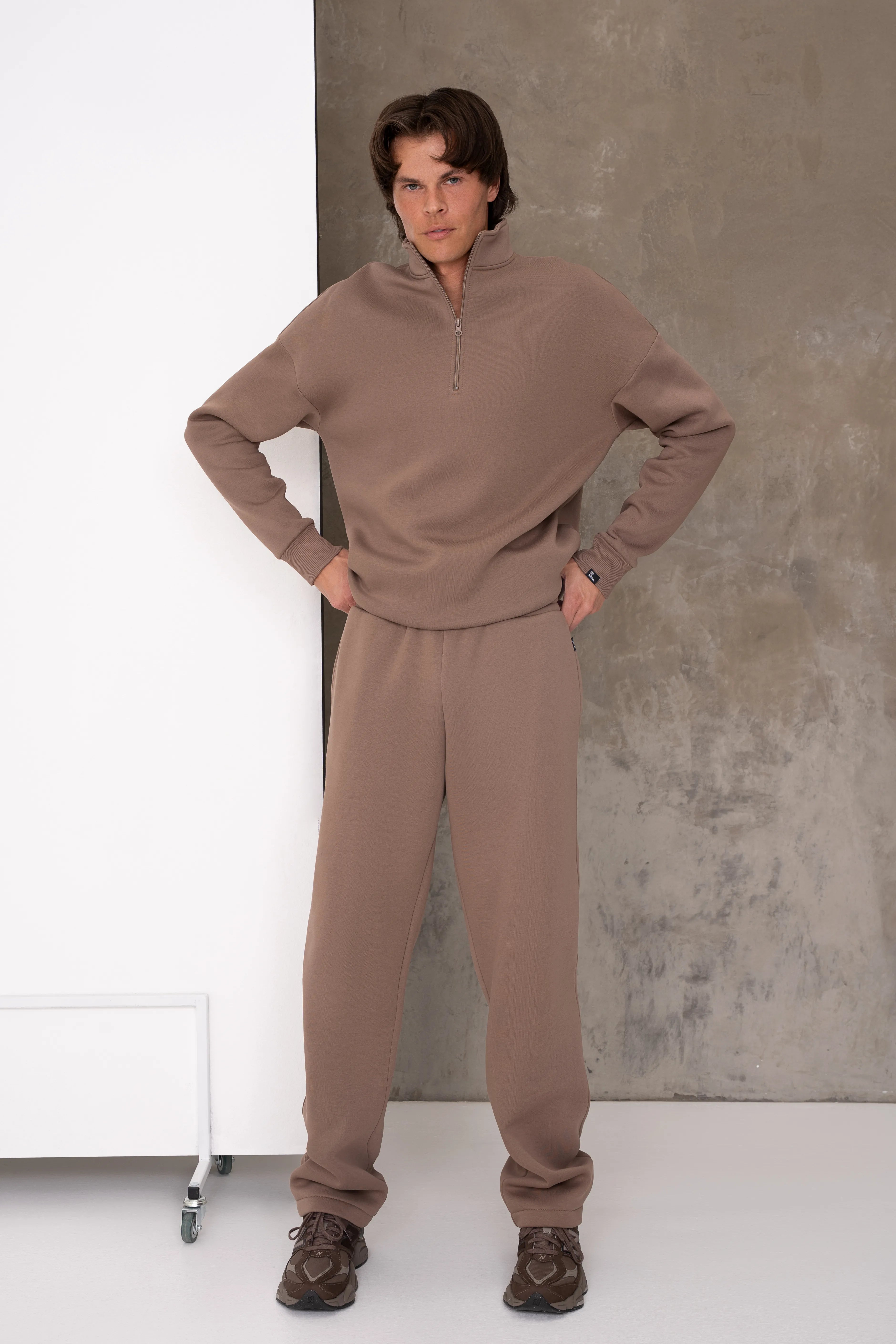 Latte spalvos vyriškas laisvalaikio treningas su laisvesnio kirpimo džemperiu, aukšta apykakle su metaliniu užtrauktuku ir tiesaus silueto kelnėmis su šoninėmis kišenėmis, pilnas vaizdas