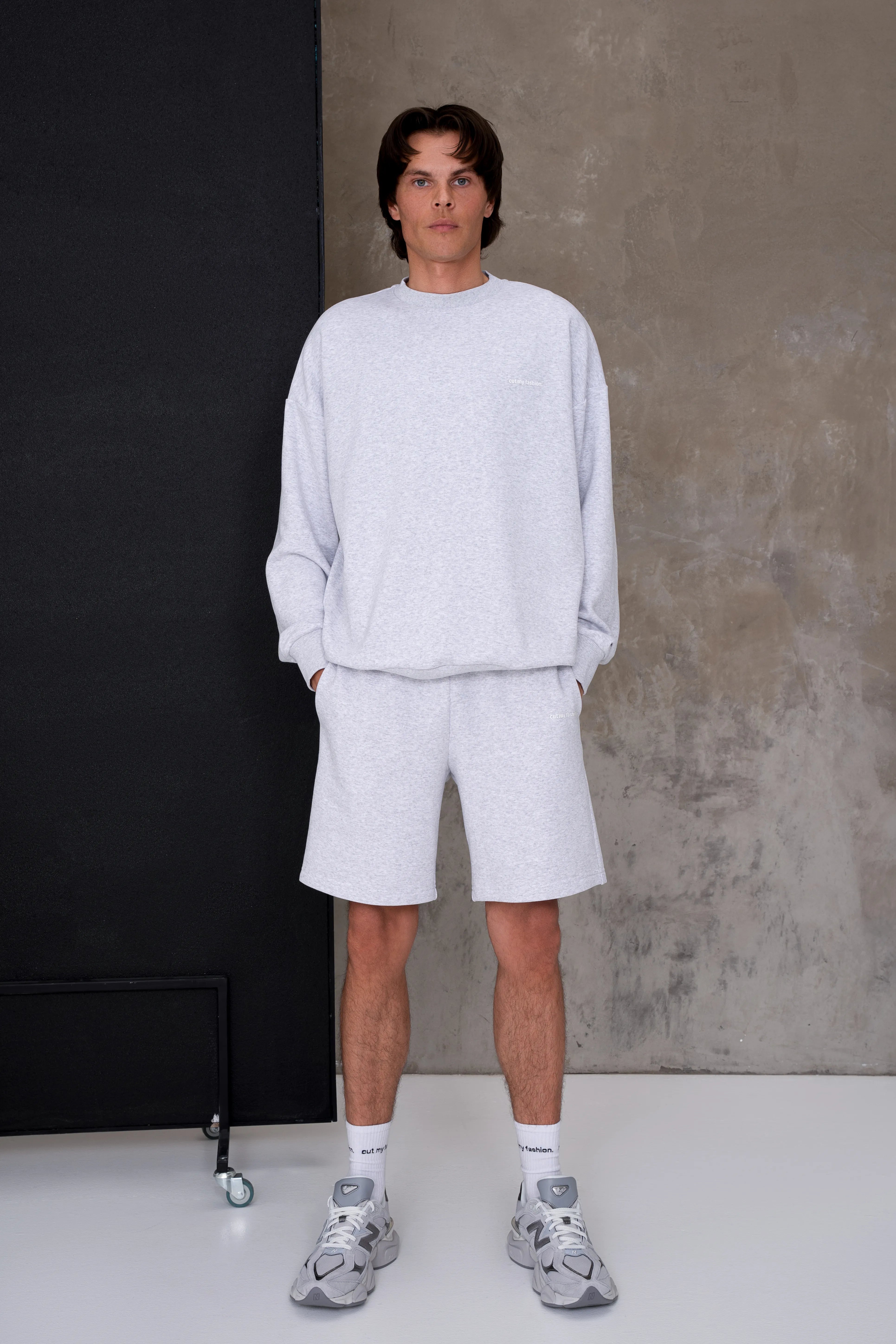 Šviesiai pilkas vyriškas laisvalaikio treningas su šortais ir laisvo silueto džemperiu, nuleista pečių linija, apvali apykaklė, elastingi rankogaliai, tiesaus kirpimo šortai su šoninėmis kišenėmis
